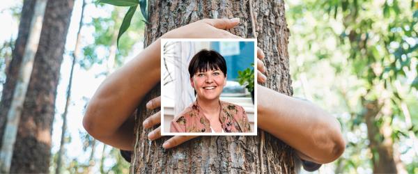 Inklippt bild på VD Susanna Strandberg framför träd som kramas av armar. 