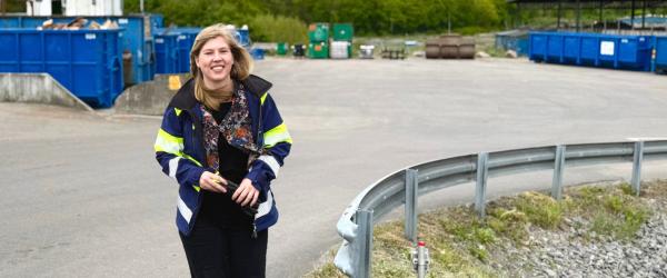 Ylva Nilsson, kommunikatör på VMAB, går med ett leende över återvinningscentralen i Mörrum, omgiven av containrar och tydlig skyltning för avfallshantering.