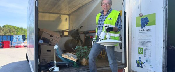 Medarbetare från Lindra visar en vit lampa vid öppen container märkt ‘Återbruket’ på återvinningscentralen.