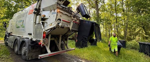 En renhållningsarbetare som drar ett kärl till en sopbil med loggan nordisk återvinning på.